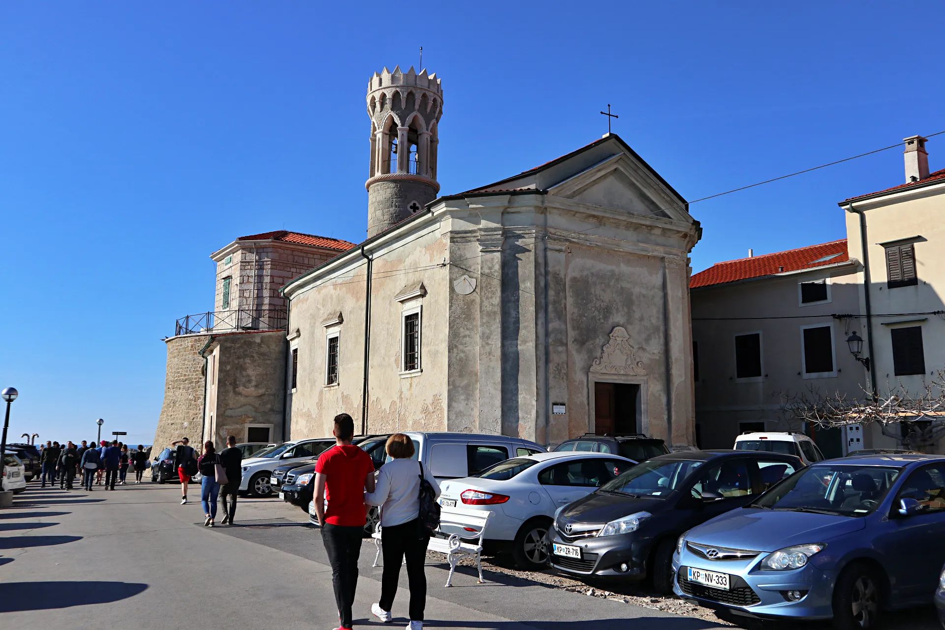 Ulica v starem jedru Pirana ob cerkvi, mimoidoči sprehajalci