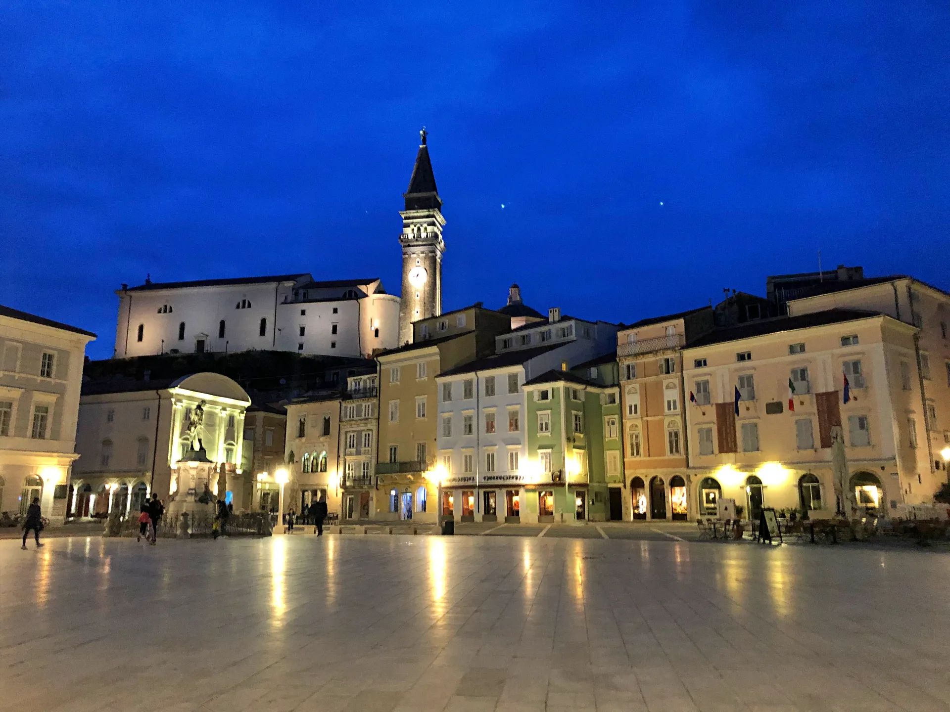 Staro mestno jedro Pirana v mraku, s toplimi lučmi ob Tartinijevem trgu in zvonikom nad strehami